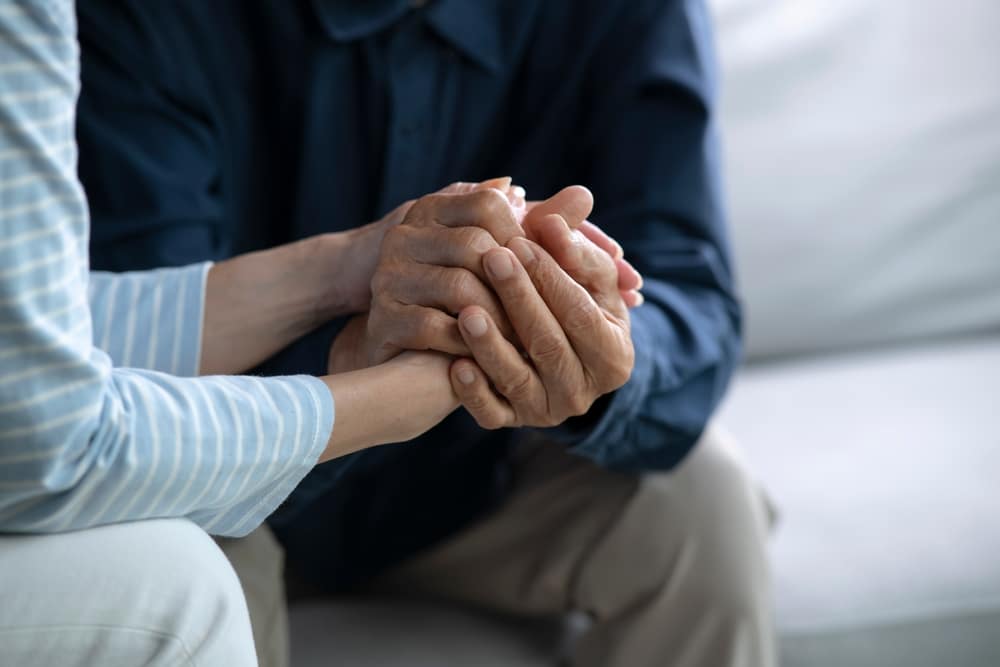 Mains d'une personne âgée et d'un aidant serrées avec tendresse pour exprimer soutien et réconfort.